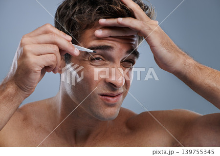 Eyebrow, studio and man with tweezers for hair removal and skincare for grooming with self care. Young model, clean and face epilation for cosmetology in cosmetics facial treatment by blue background Eyebrow, studio and man with tweezers for hair removal and skincare for grooming with self care. Young model, clean and face epilation for cosmetology in cosmetics facial treatment by blue background 139755345