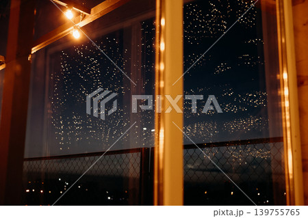 Cozy night rooftop atmosphere with hanging string lights and starry sky reflections. Warm glowing light bulbs against dark city skyline background. Magical evening terrace vibe and festive mood. Cozy night rooftop atmosphere with hanging string lights and starry sky reflections. Warm glowing light bulbs against dark city skyline background. Magical evening terrace vibe and festive mood. 139755765