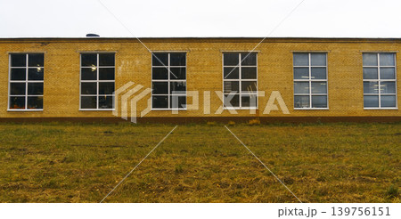 Minimalist industrial architecture. Industrial style building with repetitive windows and open lawn Minimalist industrial architecture. Industrial style building with repetitive windows and open lawn 139756151