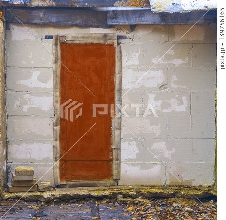 Derelict urban entrance. Deserted door set in fractured wall covered with weathered paint and debris Derelict urban entrance. Deserted door set in fractured wall covered with weathered paint and debris 139756165