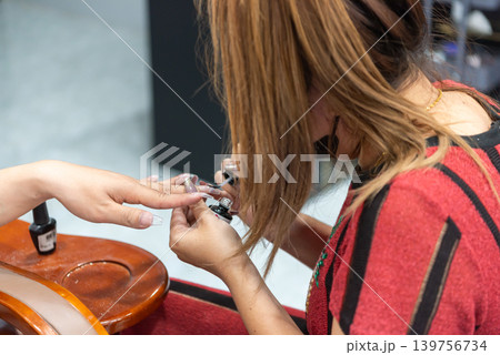Nail technician applying gel polish during manicure session highlighting beauty treatment grooming salon care service 139756734