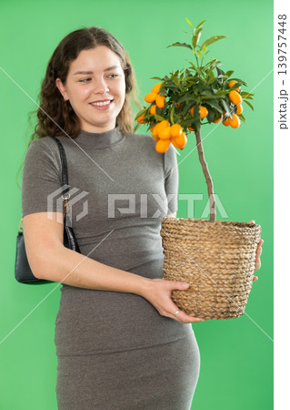 Portrait of happy girl in long dress with kumquat plant in her hands on green background 139757448