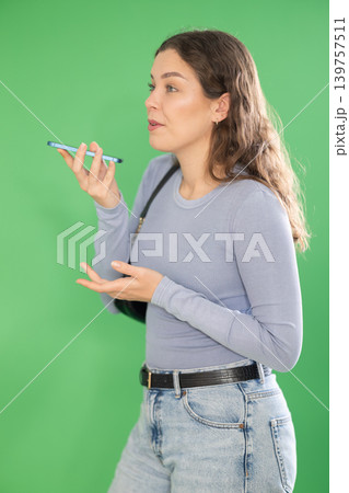 Young woman recording voice message in front of green screen Young woman recording voice message in front of green screen 139757511