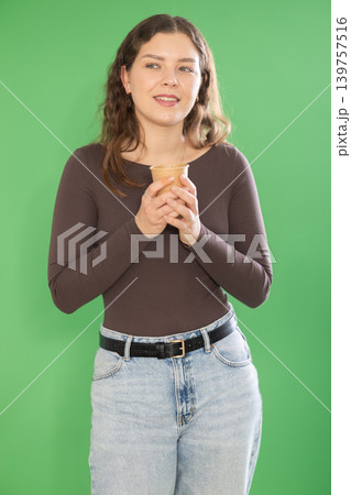 Young woman scrolling smartphone and drinking coffee in front of green screen Young woman scrolling smartphone and drinking coffee in front of green screen 139757516