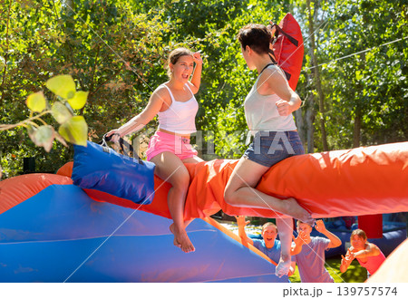 Happy girl funny pillow fighting on inflatable log with female friend 139757574