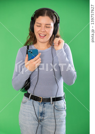 Young woman listening to music with headphones in front of green screen Young woman listening to music with headphones in front of green screen 139757627
