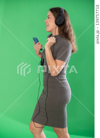 Young woman listening to music with headphones in front of green screen 139757718