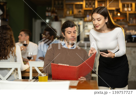 Girl waiter communicates with male customer, answers questions about composition of dish of day Girl waiter communicates with male customer, answers questions about composition of dish of day 139757727