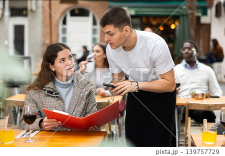 On open area of cafe, guy waiter communicates with girl customer, accepts order 139757729