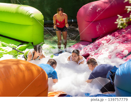 Cheerful friends picking up balls in inflatable pool full of foam 139757779
