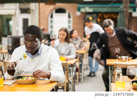 On open area of cafe, African man in restaurant eating salad 139757809