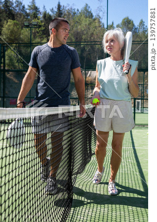 Man and elderly woman walking along tennis net on open court after match 139757881