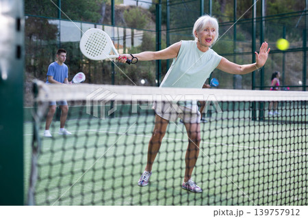 Active elderly woman playing padel tennis on open court 139757912