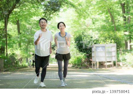 新緑の公園でジョギングやランニング、ウォーキングを楽しむ健康的な走る夫婦の運動ライフスタイル全身 139758041