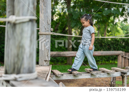 preschool child girl walking on a wooden balancing bridge at outdoor playground 139758199