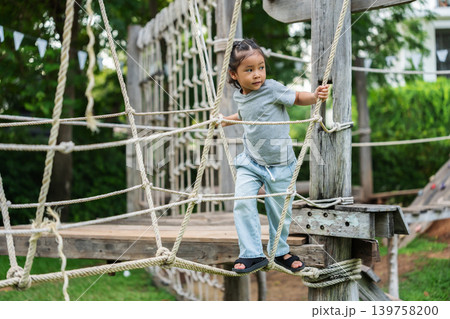 preschool child girl playing and walking on wooden rope bridge at outdoor playground in park 139758200