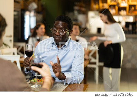 African man in cafe sits opposite male companion, has nice conversation African man in cafe sits opposite male companion, has nice conversation 139758566