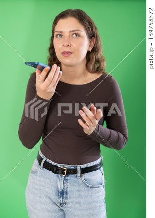 Young woman recording voice message in front of green screen Young woman recording voice message in front of green screen 139758572