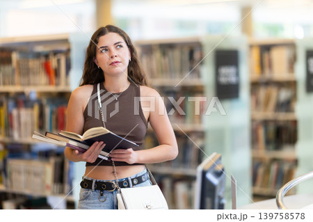 Young female student reading book in library 139758578