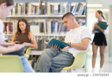 Male student reading book on chair in library 139758597