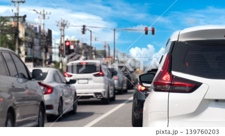 Vehicles are tightly packed in a traffic jam at a city intersection under a blue sky with light clouds. White SUV is prominent in the foreground waiting behind a long line of cars near traffic signal. Vehicles are tightly packed in a traffic jam at a city intersection under a blue sky with light clouds. White SUV is prominent in the foreground waiting behind a long line of cars near traffic signal. 139760203