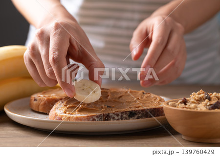 Woman's hands preparing a healthy breakfast, cranberry sourdough bread with peanut butter and banana Woman's hands preparing a healthy breakfast, cranberry sourdough bread with peanut butter and banana 139760429
