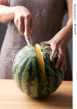 Woman's hands holding a knife and cutting a fresh yellow watermelon on a wooden cutting board 139760440