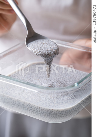 Chia seeds soaking in milk in a glass bowl with spoon holding by hand Chia seeds soaking in milk in a glass bowl with spoon holding by hand 139760473