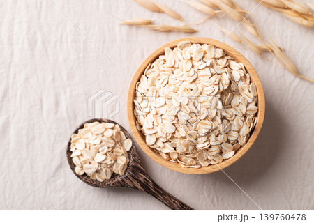 Dried rolled oat flake in a wooden bowl and spoon on white background Dried rolled oat flake in a wooden bowl and spoon on white background 139760478