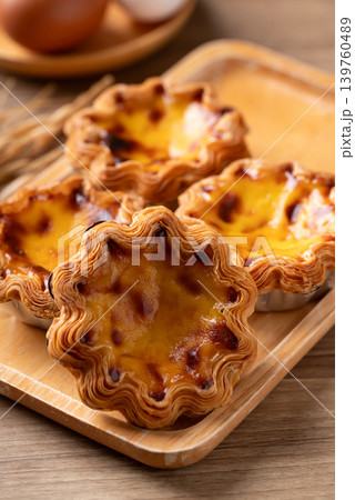 Egg tarts filled with creamy custard and caramelized tops on a wooden plate Egg tarts filled with creamy custard and caramelized tops on a wooden plate 139760489