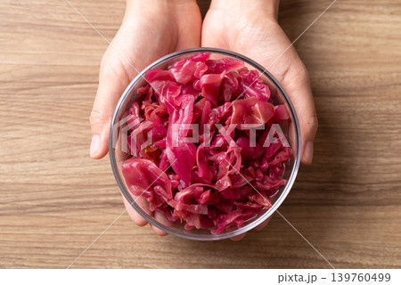Red cabbage sauerkraut in a glass bowl holding by woman hand on wooden background Red cabbage sauerkraut in a glass bowl holding by woman hand on wooden background 139760499