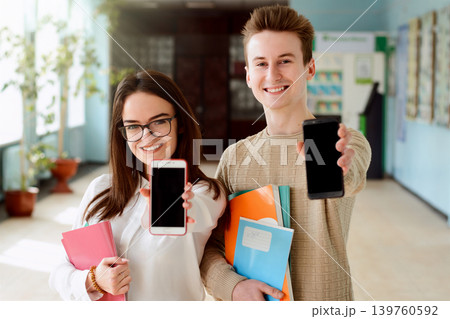 Young smiling freshers showing screens of their smartphones to the camera happy to receive message about entering desired leading university ready to study hard and achieve high results 139760592