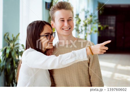 Young female and male students gossiping and bulling on somebudy in corridor of the college. Two friends sharing secrets about their classmate point her and laugh at her during the break 139760602