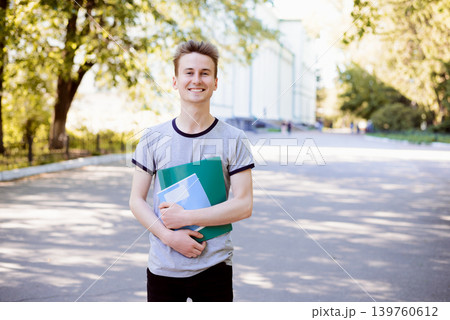 Cheerful young student with folder and exercise books enjoying walk in the park near university in the evening after classes Cheerful young student with folder and exercise books enjoying walk in the park near university in the evening after classes 139760612