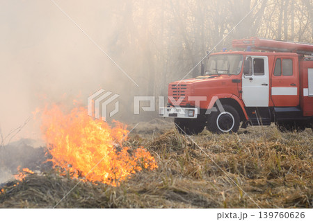 Fire truck near burning grass in countryside has come to put out a wild fire Fire truck near burning grass in countryside has come to put out a wild fire 139760626
