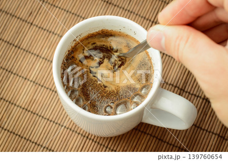 Man`s hand stirs coffee with a spoon. Making coffee in the morning. Man`s hand stirs coffee with a spoon. Making coffee in the morning. 139760654