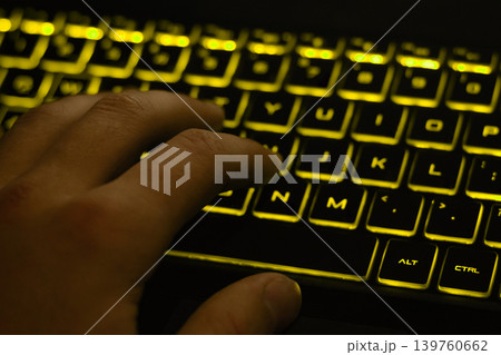 Man's hand typing on keyboard with yellow backlight Man's hand typing on keyboard with yellow backlight 139760662