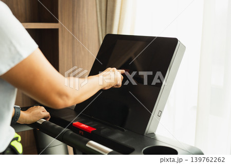 Woman setting on a treadmill's touchscreen before starting a cardio workout. Woman setting on a treadmill's touchscreen before starting a cardio workout. 139762262