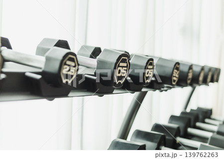 A row of black dumbbells on a storage rack in a fitness center. 139762263