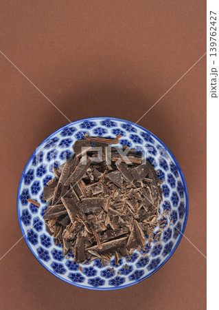 Chopped dark chocolate in a blue patterned bowl on brown background 139762427