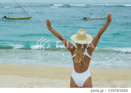 Woman stands on the beach with arms raised toward the ocean 139763088