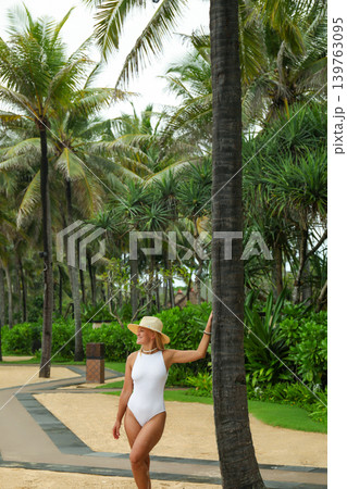Woman stands by a palm tree in a tropical setting Woman stands by a palm tree in a tropical setting 139763095