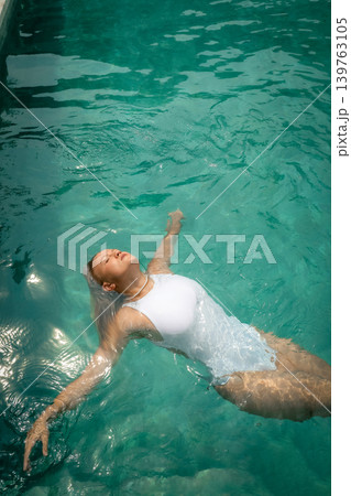 Woman floats in a pool enjoying warm weather in Bali Woman floats in a pool enjoying warm weather in Bali 139763105