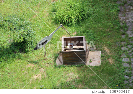 Traditional wooden water well with a decorative stork crane in a green garden Traditional wooden water well with a decorative stork crane in a green garden 139763417