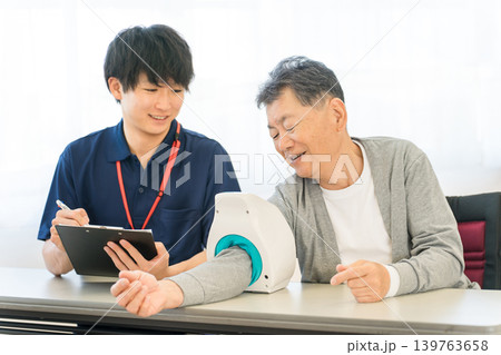 血圧計を使い血圧測定をするシニア男性と記録をとる看護師,介護士の男性スタッフ 血圧計を使い血圧測定をするシニア男性と記録をとる看護師,介護士の男性スタッフ 139763658