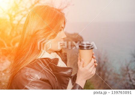 Woman coffee sunset young lady in leather jacket holding a paper cup and looking at the ocean at dusk with copy space Woman coffee sunset young lady in leather jacket holding a paper cup and looking at the ocean at dusk with copy space 139763891