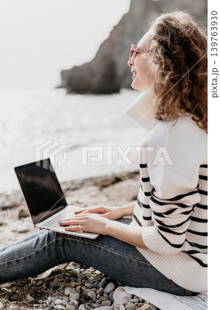 Laptop woman beach young smiling freelancer working on a laptop while sitting on a rocky shore near the ocean Laptop woman beach young smiling freelancer working on a laptop while sitting on a rocky shore near the ocean 139763930
