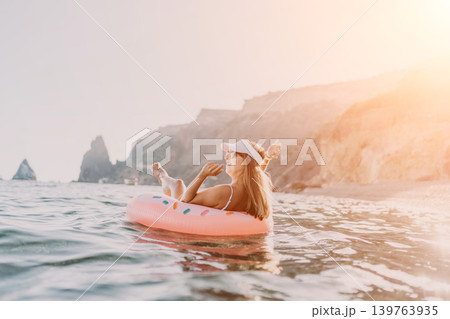 Woman beach ocean. Happy woman relaxing on inflatable donut ring in the sea with scenic cliffs. Woman beach ocean. Happy woman relaxing on inflatable donut ring in the sea with scenic cliffs. 139763935