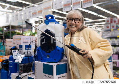 Senior woman at hardware store choosing a battery powered garden sprayer Senior woman at hardware store choosing a battery powered garden sprayer 139765486