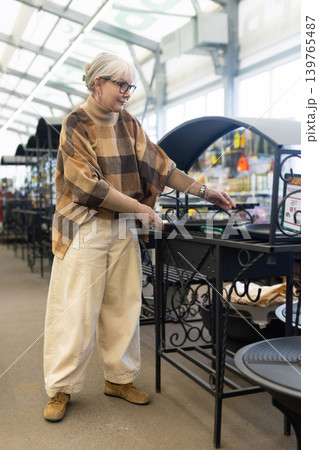 Senior woman examining barbecue grill while shopping in a hardware store Senior woman examining barbecue grill while shopping in a hardware store 139765487